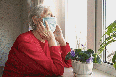 Une personne âgée seule à sa fenêtre et portant un masque buccal 